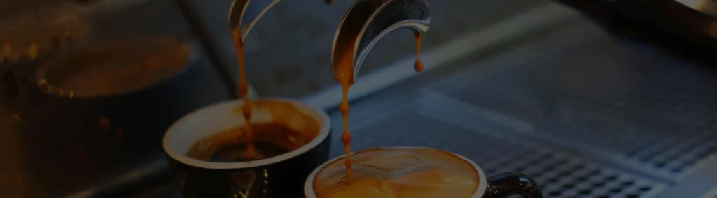 Dos tazas de café espresso siendo llenadas desde una máquina de café