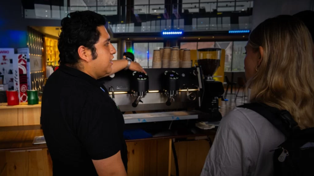 Café orgánico en Latinoamérica Barista mostrando el funcionamiento de una máquina de café a un cliente en una cafetería