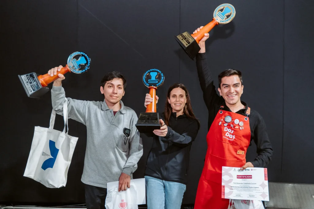 Tres baristas sosteniendo trofeos y certificados en un evento de café