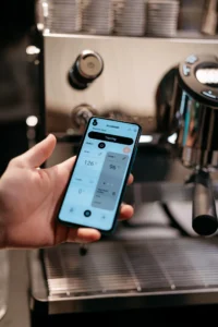 Persona usando un teléfono móvil para controlar una máquina de café profesional