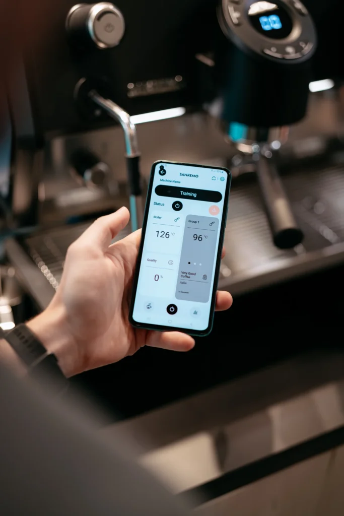 maquinaria para cafeterías
Persona sosteniendo un teléfono con la interfaz de control de una máquina de café profesional